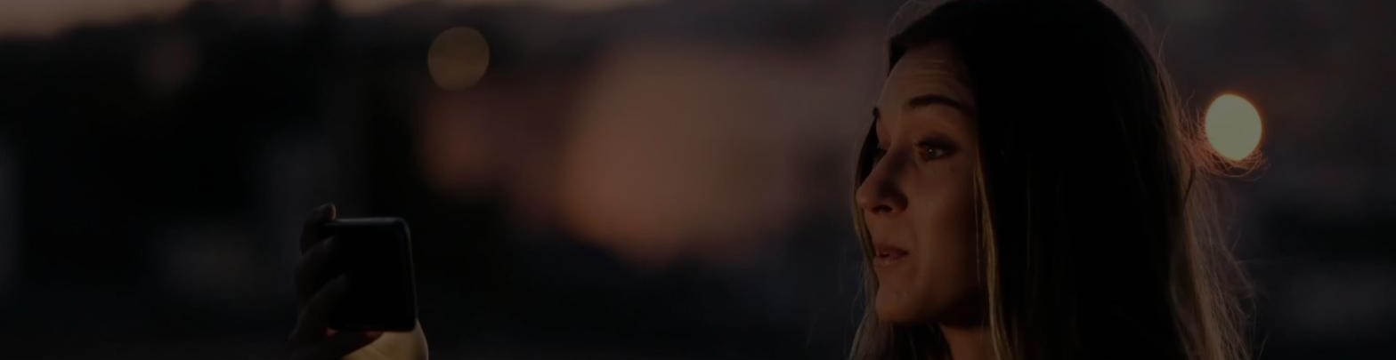 A woman at dusk recording a video response on her phone, from the fabric.is homepage.