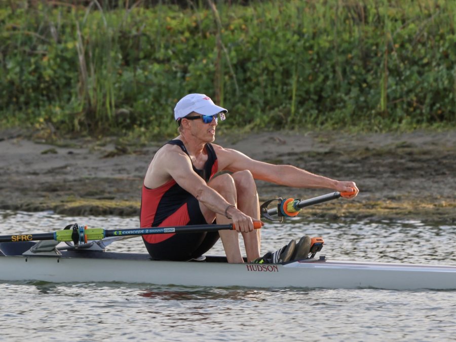 Tom rowing a single scull, mid-stroke, in a red and black racing suit.